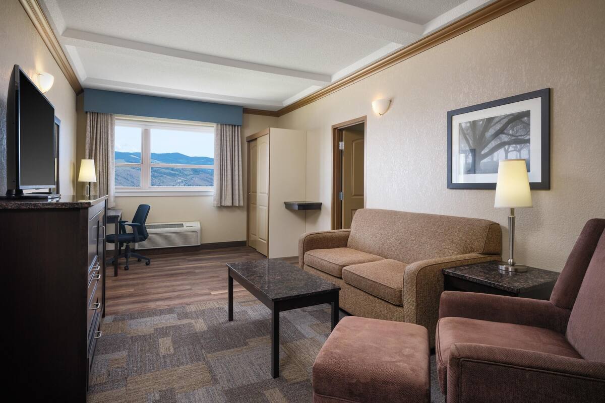 A hotel room with a sofa, armchair, desk, and TV.