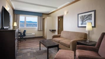 Habitación de hotel con sofá, sillón, escritorio y televisión.