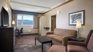 Habitación de hotel con sofá, sillón, escritorio y televisor.