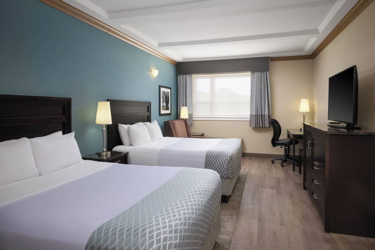 A hotel room with two beds, a desk, a chair, a television, and a dresser.