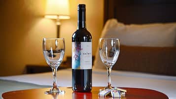 A bottle of Merlot wine, two empty wine glasses, and a small packet of cigarettes on a wooden table in a hotel room.