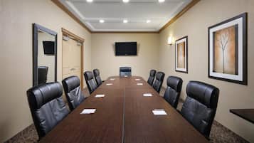 A conference room with a long table, black leather chairs, a flat-screen TV, and framed artwork on the walls.