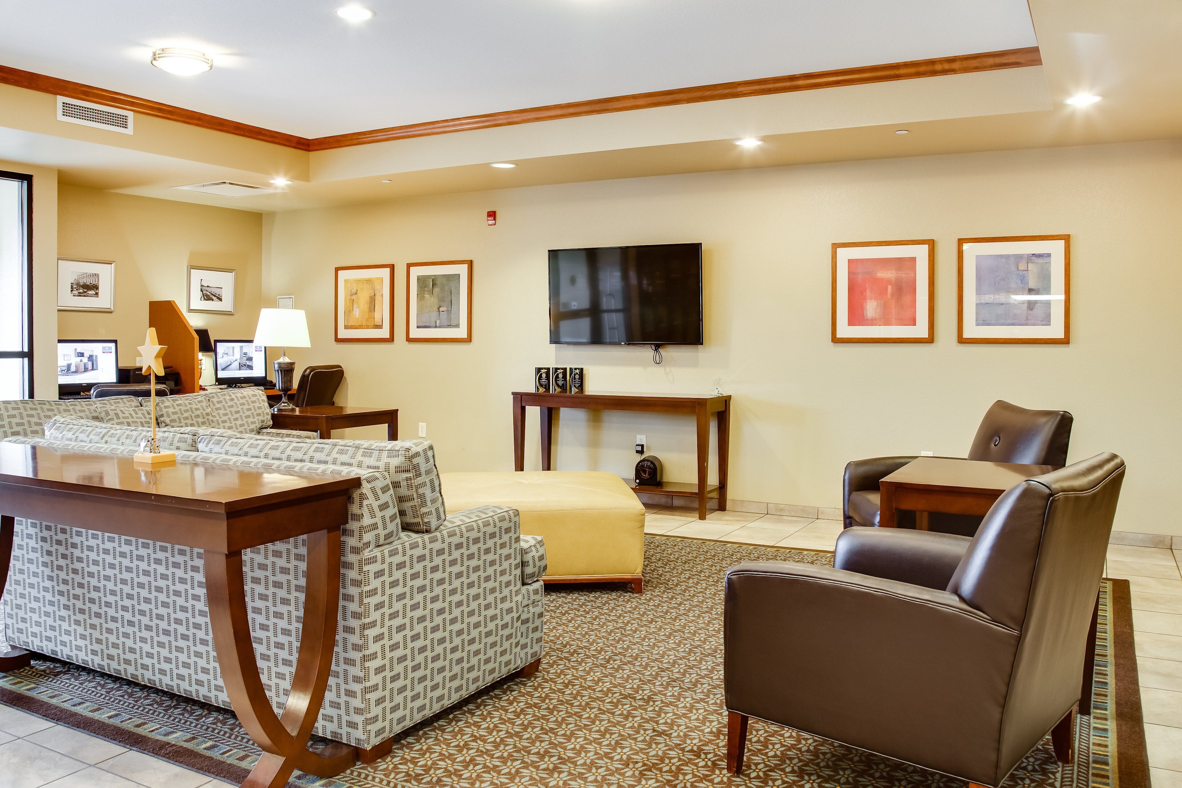Habitación de hotel con sofá, una mesa de comedor, televisión montada en la pared y cuadros enmarcados.
