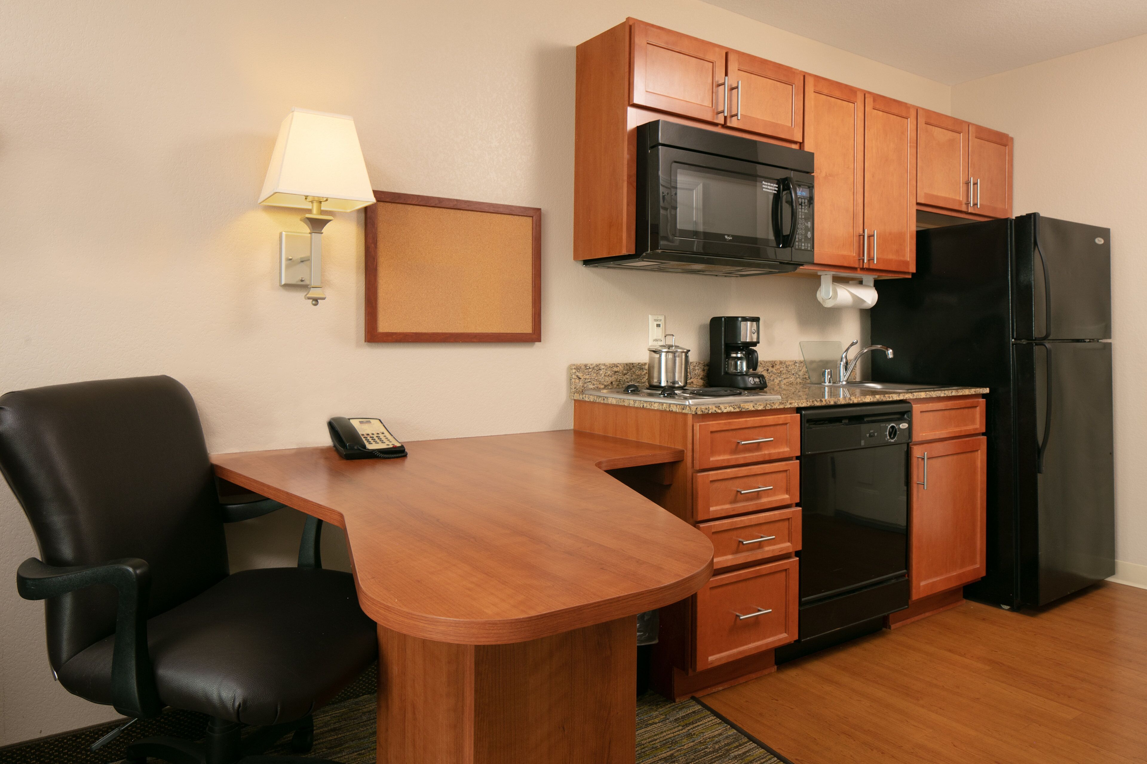 Cocina compacta con microondas, refrigerador, cafetera y un pequeño comedor con una silla y mesa.