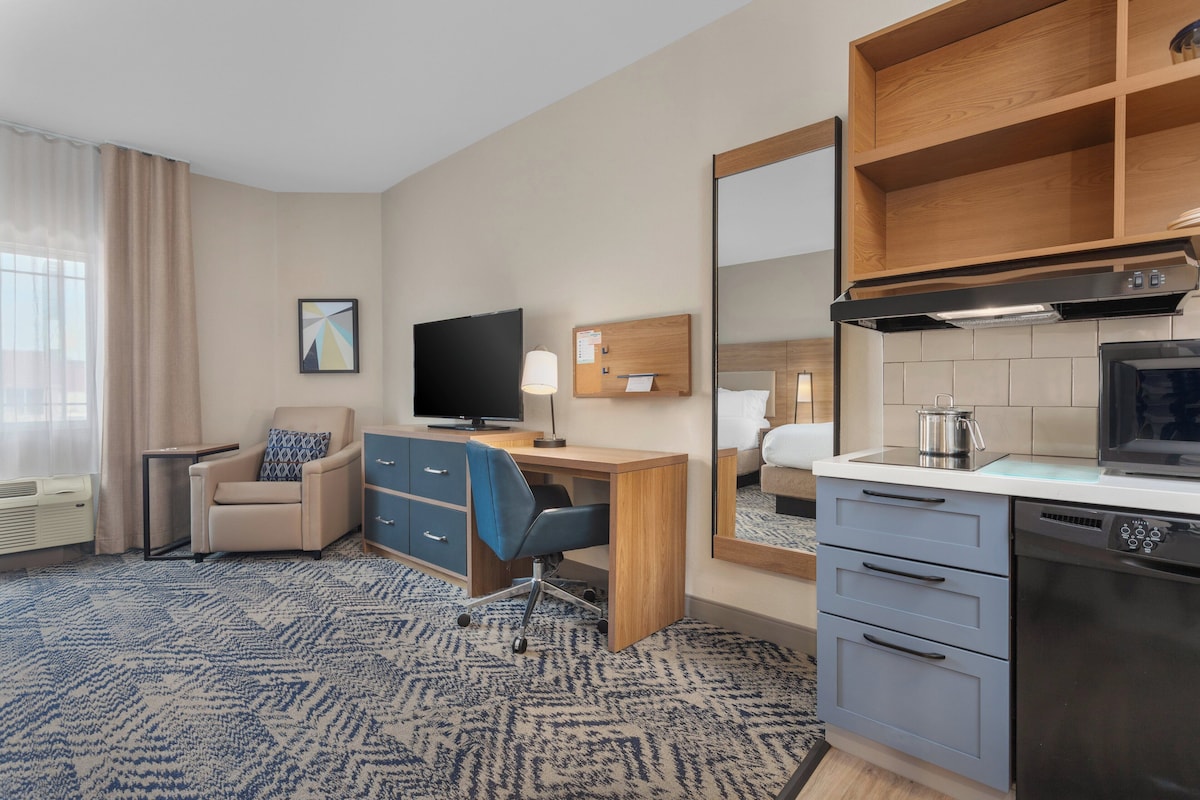 A hotel room with a desk, chair, television, and kitchenette.