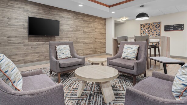 Un hall d’entrée moderne avec des fauteuils à revêtement gris, une table basse ronde en bois et un téléviseur à écran plat fixé à un mur en bois.