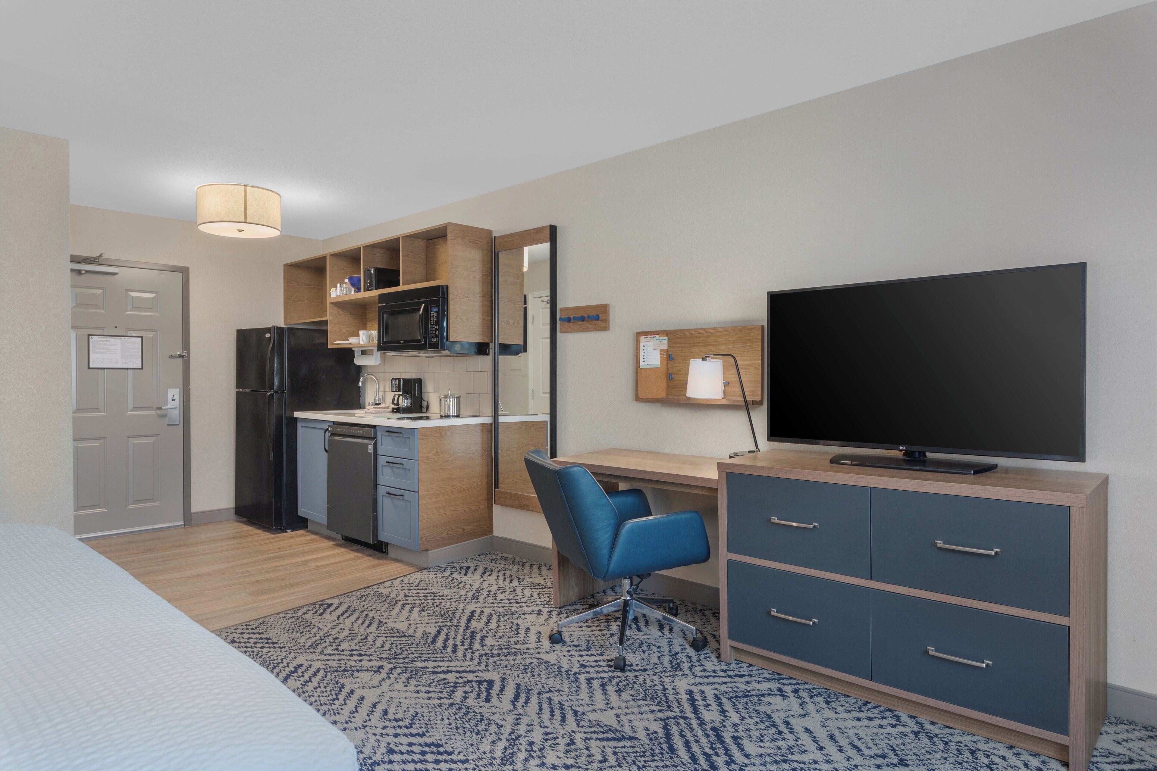 Habitación de hotel con cama, escritorio y silla, televisión, kitchenette y baño.