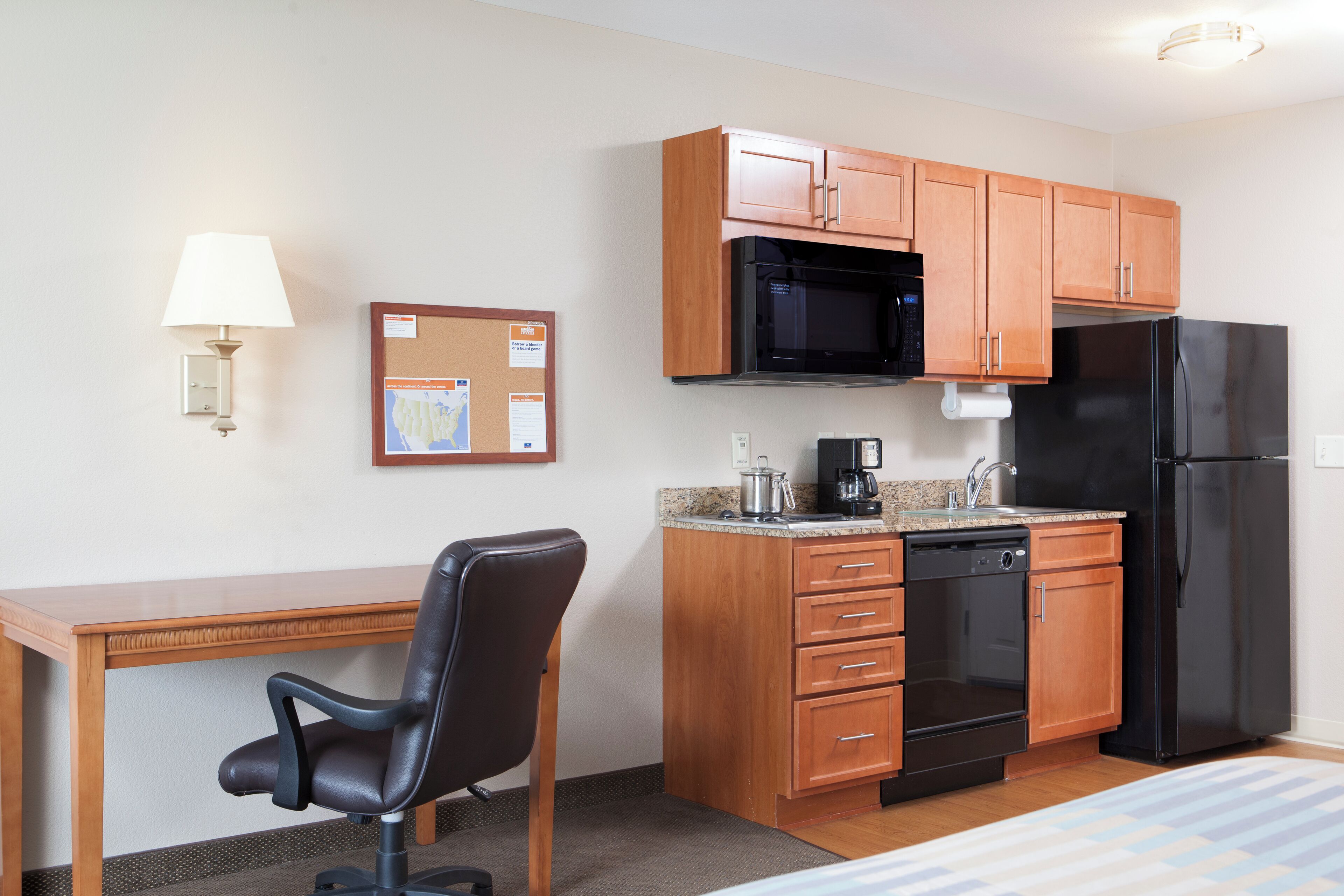 Habitación de hotel compacta con kitchenette, un escritorio de madera, una silla de oficina negra, microondas, refrigerador y cafetera.