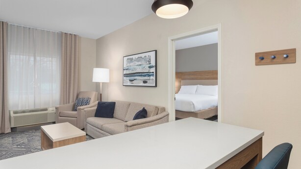 A hotel room with a bed, a desk, a chair, a sofa, a lamp, a painting, and a wall-mounted light fixture.