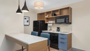 Une cuisine moderne avec un plan de travail blanc, des appareils électroménagers noirs et des chaises bleues.
