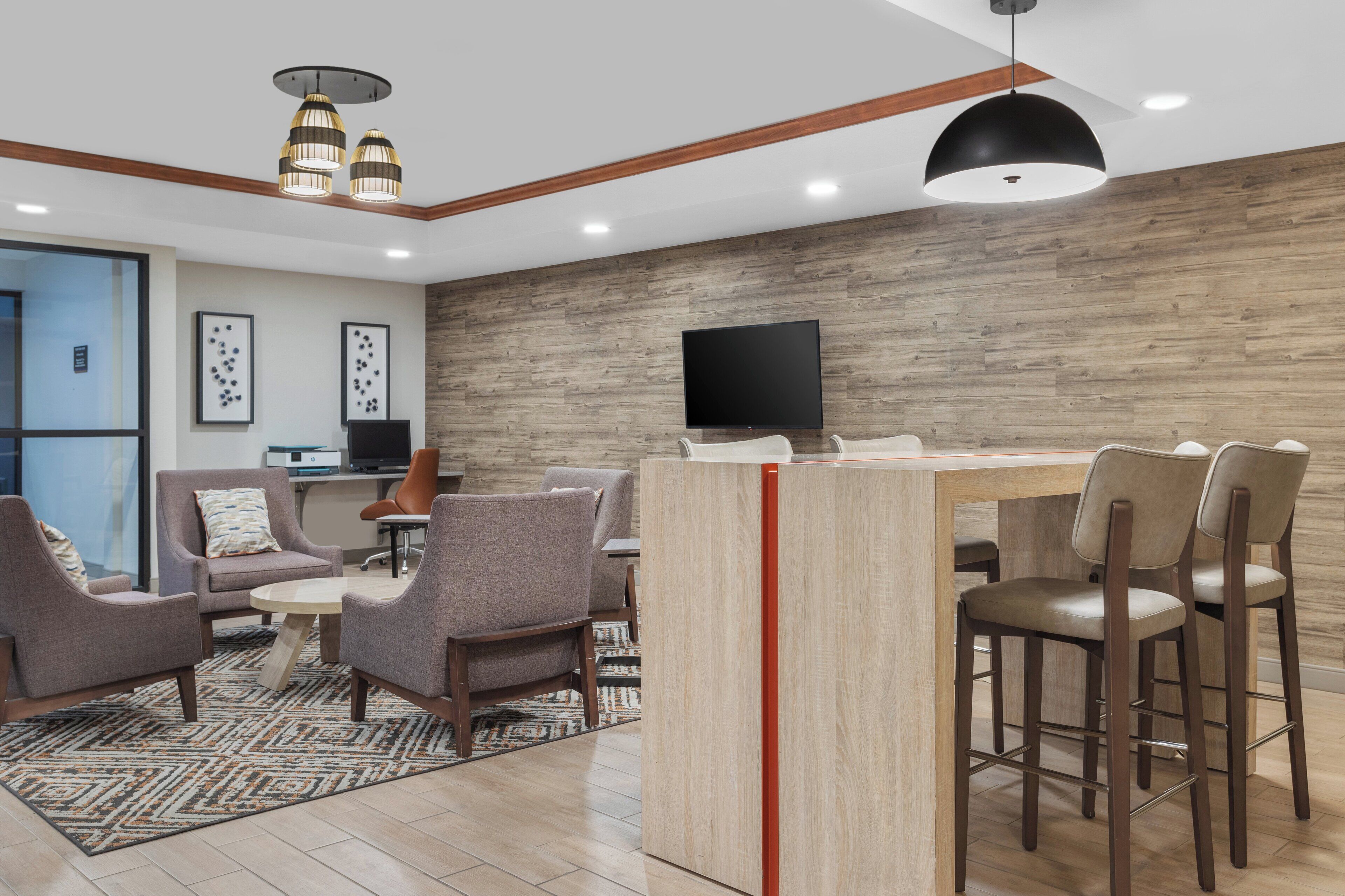 A modern living room with a wooden accent wall, a flat-screen TV, and a bar area with stools.