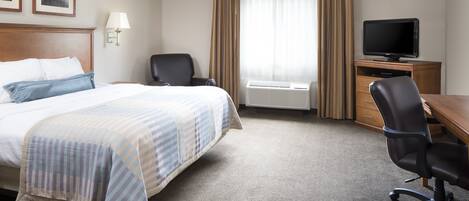 Ein Hotelzimmer mit einem großen Bett, einem Schreibtisch mit Computer, einem Sessel, einem Fernseher und einem Fenster mit Vorhängen.