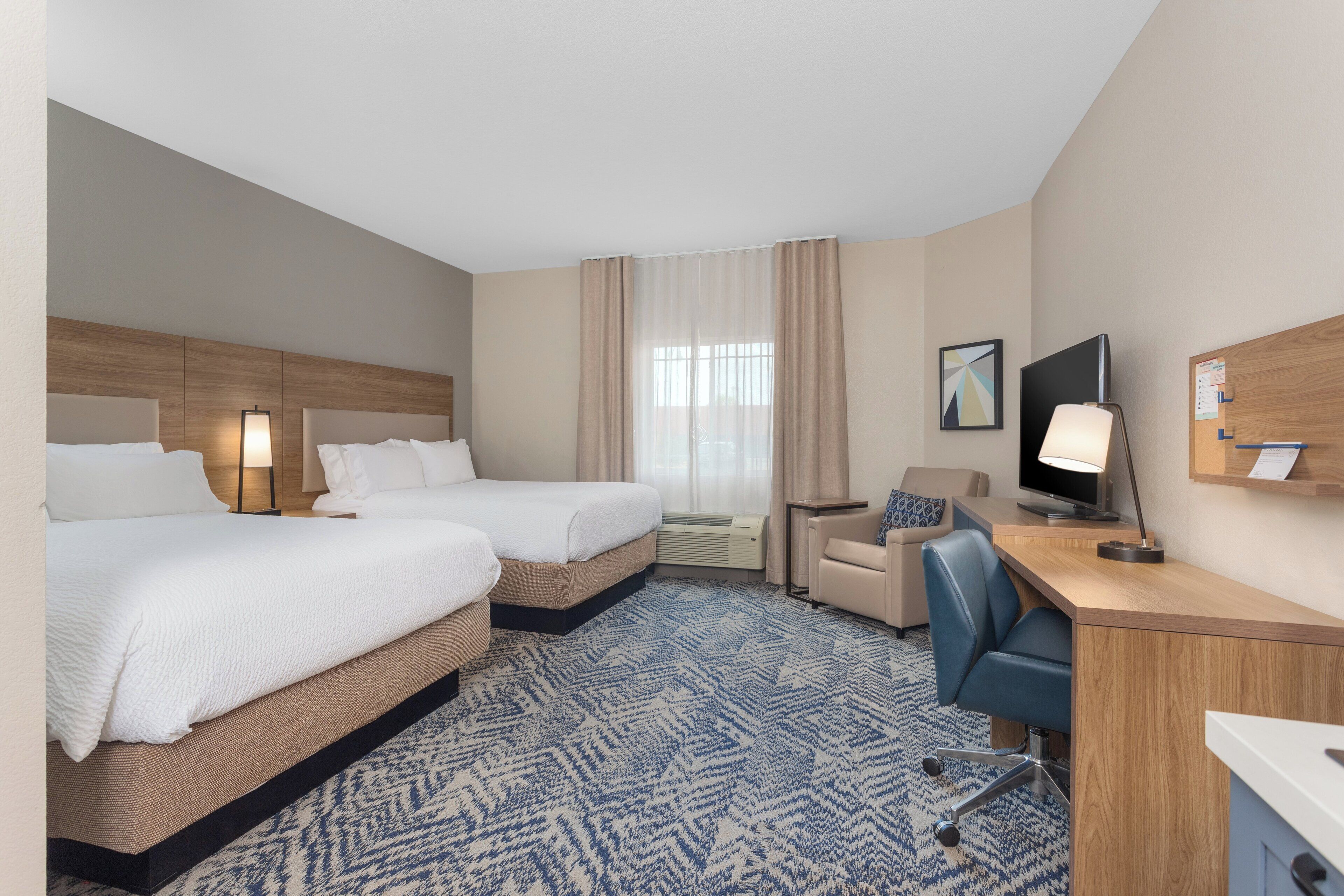 A hotel room with two beds, a desk, a chair, a television, and a window with curtains.