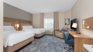 A hotel room with two beds, a desk, a chair, a television, and a window with curtains.