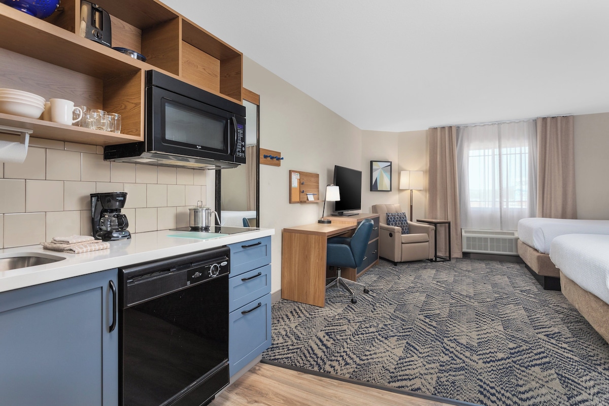 A hotel room with a kitchenette, a bed, a desk, and a TV.