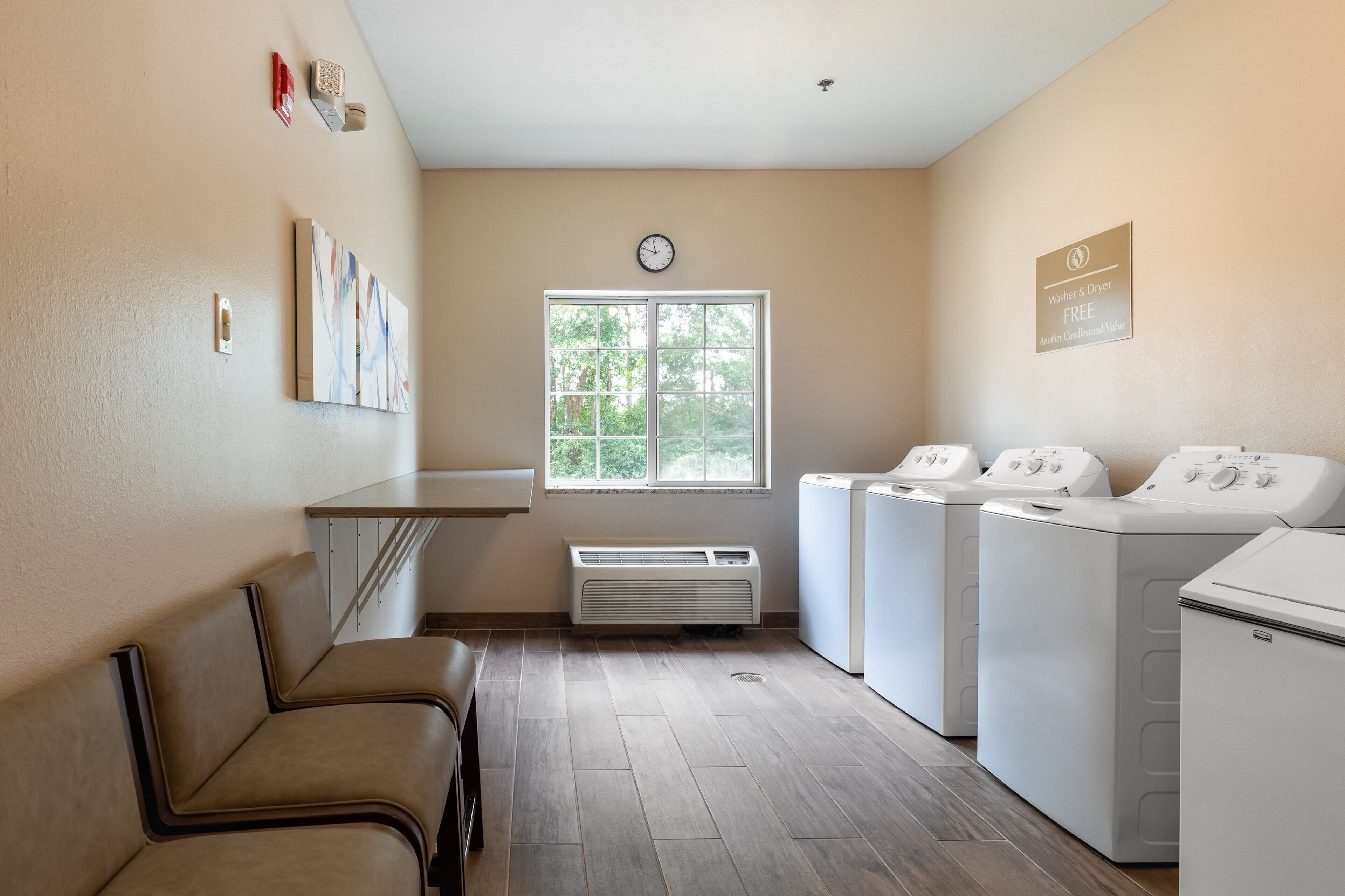 A laundry room with a bench, a large window, and multiple washing machines.
