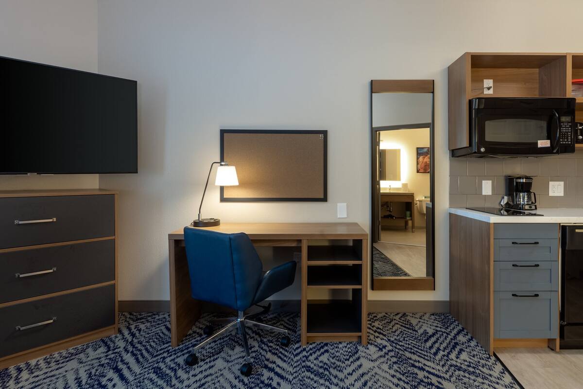 Habitación de hotel con escritorio, silla, televisión de pantalla plana, microondas y una pequeña kitchenette.