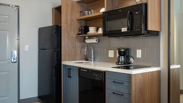 A modern kitchen with a built-in dishwasher, a black refrigerator, a microwave, and a coffee maker.