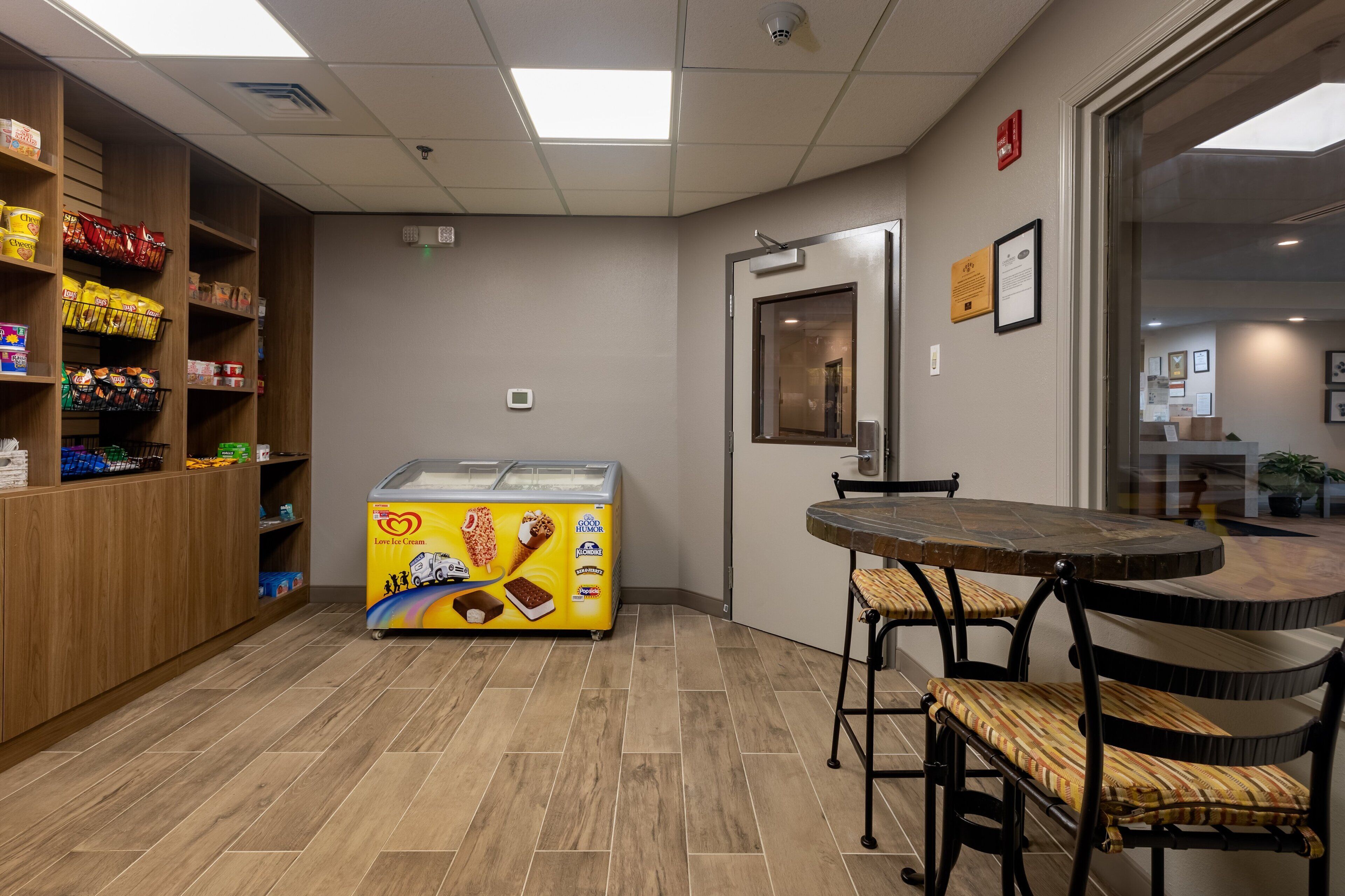 Een foodcourt met een toonbank waarop diverse snacks staan en een vriezer met ijs. Er staan stoelen en een tafel in het midden.