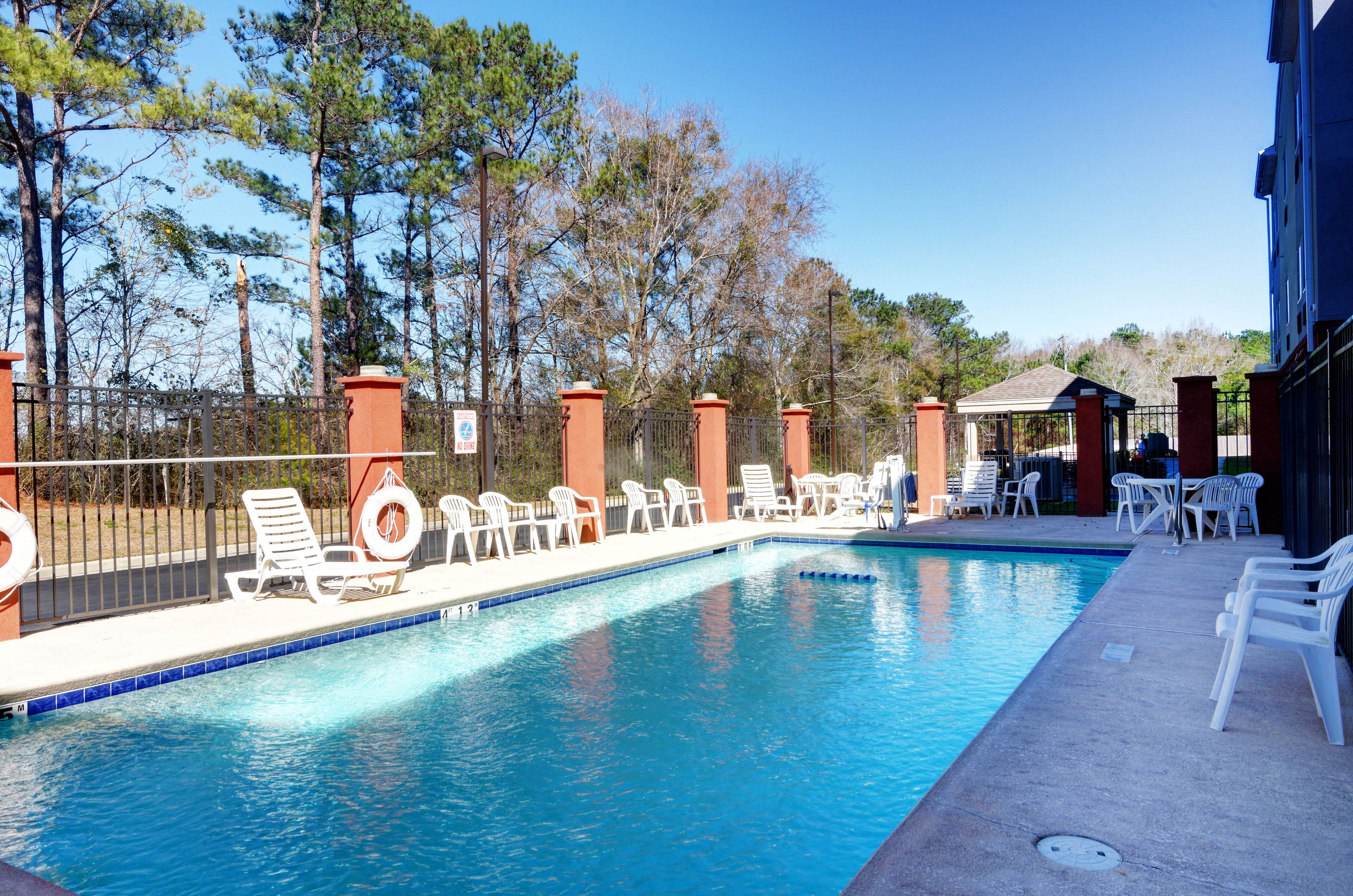 A swimming pool with lounge chairs and a fence, surrounded by trees.