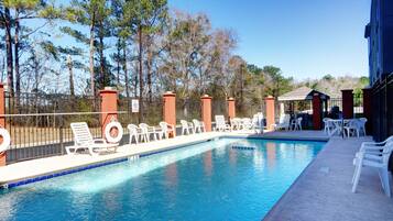 A swimming pool with lounge chairs and a fence, surrounded by trees.