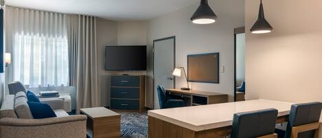 A modern hotel room with a sofa, a desk, a chair, a TV, and a large mirror.