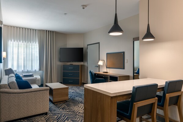 A modern hotel room with a sofa, a desk, a chair, a TV, and a large mirror. - Candlewood Suites Enterprise by IHG (Enterprise)