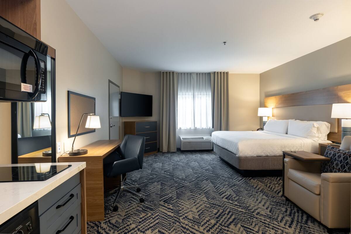 Una habitación de hotel con cama, escritorio, silla, televisión y un ventanal con cortinas.
