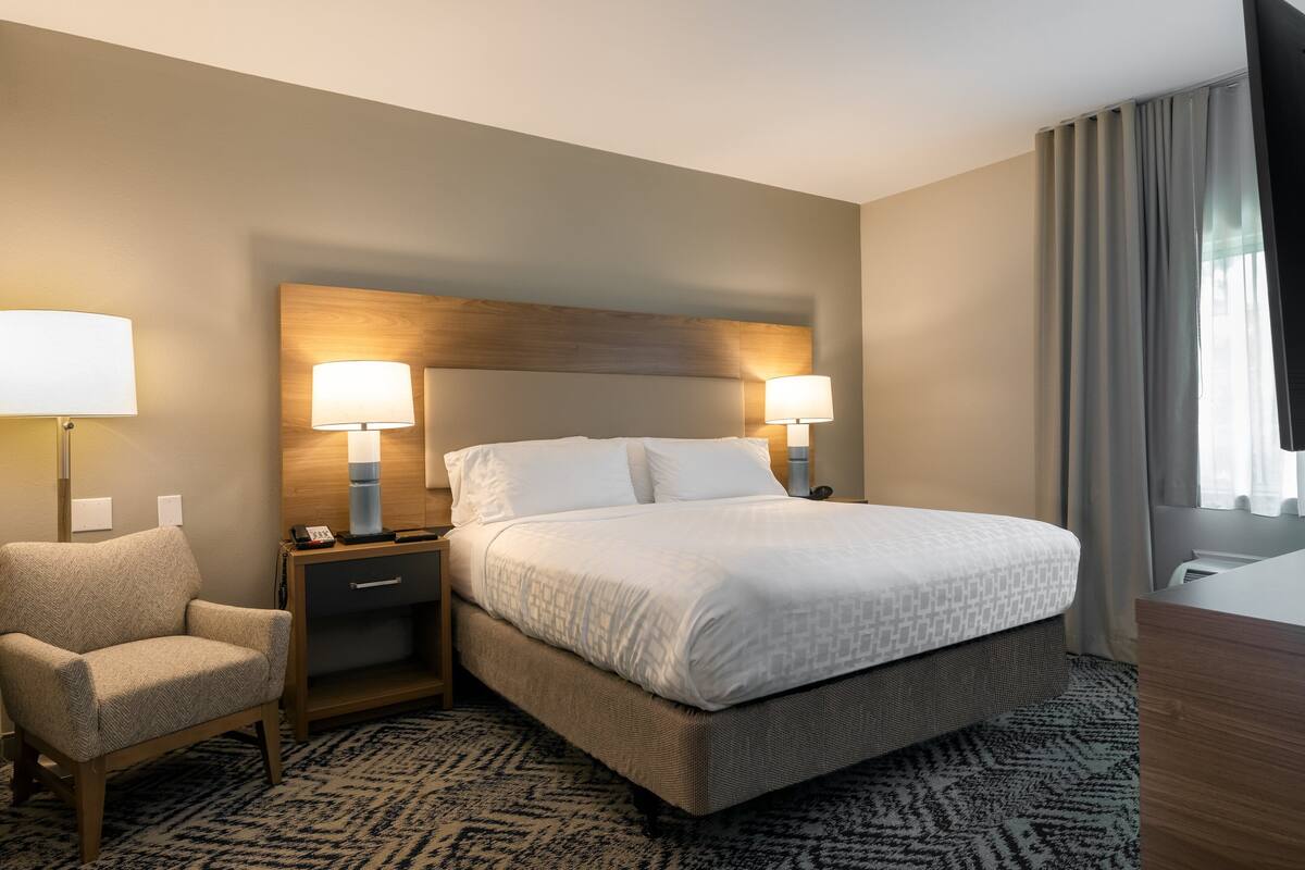 Habitación de hotel con una cama grande, dos lámparas de noche, una silla, una mesita de noche y una alfombra estampada.