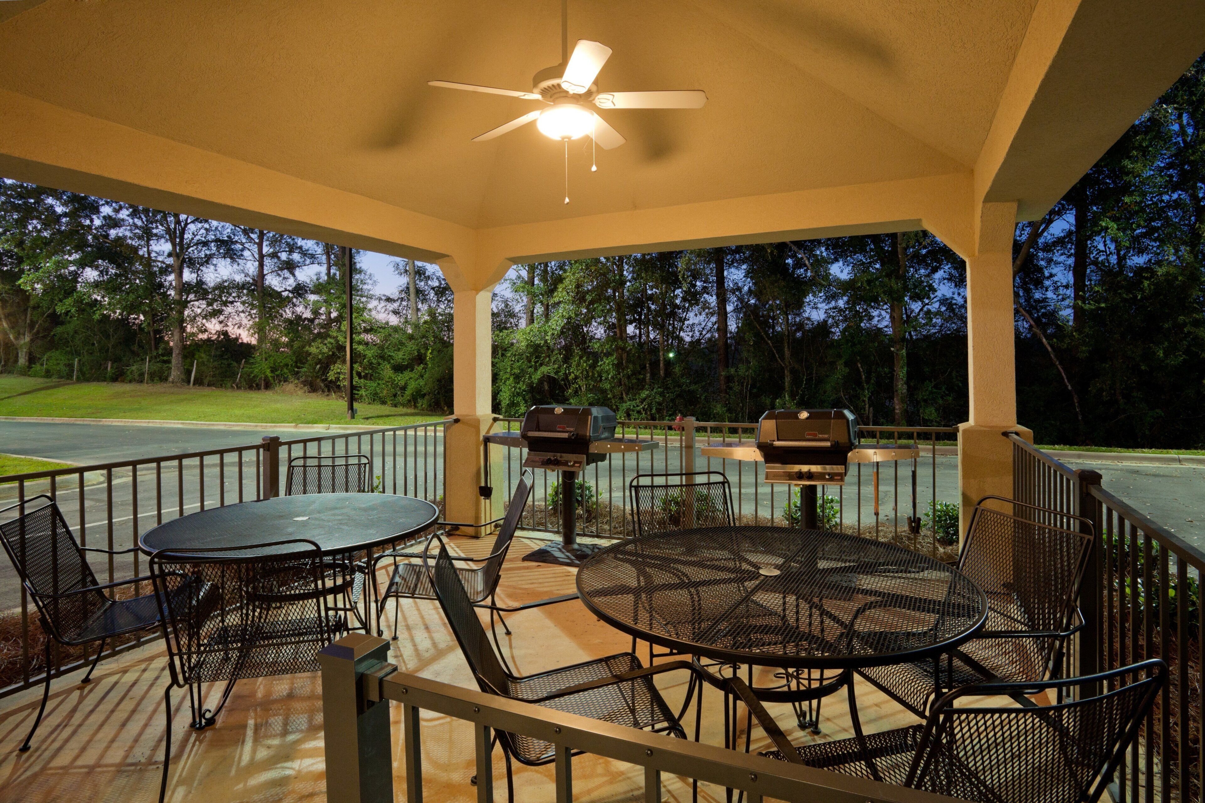 An outdoor patio with a round table and chairs, a ceiling fan, and two barbecue grills.
