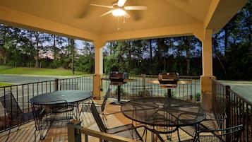 An outdoor patio with a round table and chairs, a ceiling fan, and two barbecue grills.