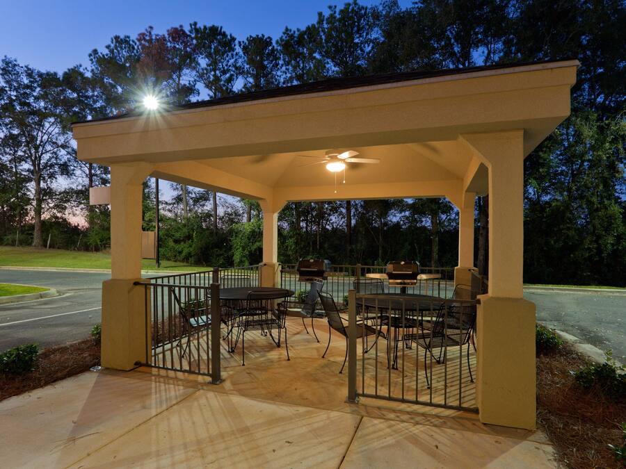 A covered outdoor patio with tables and chairs, a ceiling fan, and a view of the surrounding trees.