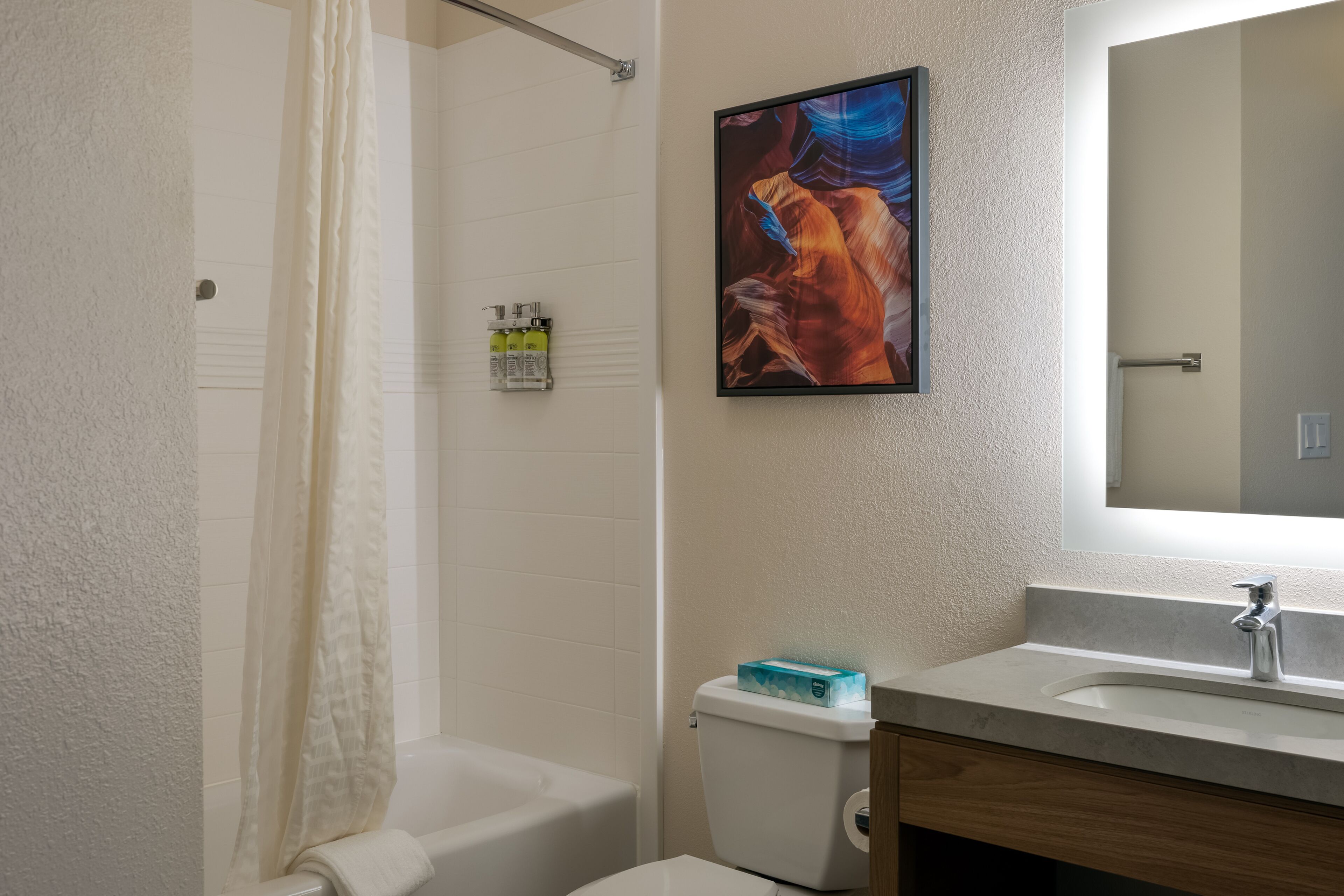 Een badkamer met een bad, toilet, wastafel en een ingelijst schilderij aan de muur.