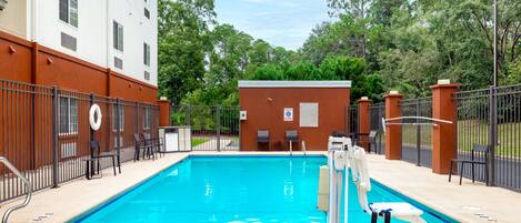 A swimming pool with a lifeguard chair, a lifeguard stand, and a small building in the background.