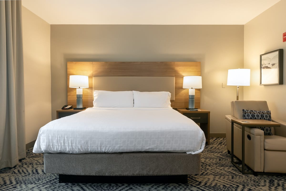 Una habitación de hotel con una cama grande, dos lámparas de noche, una silla y una mesita.