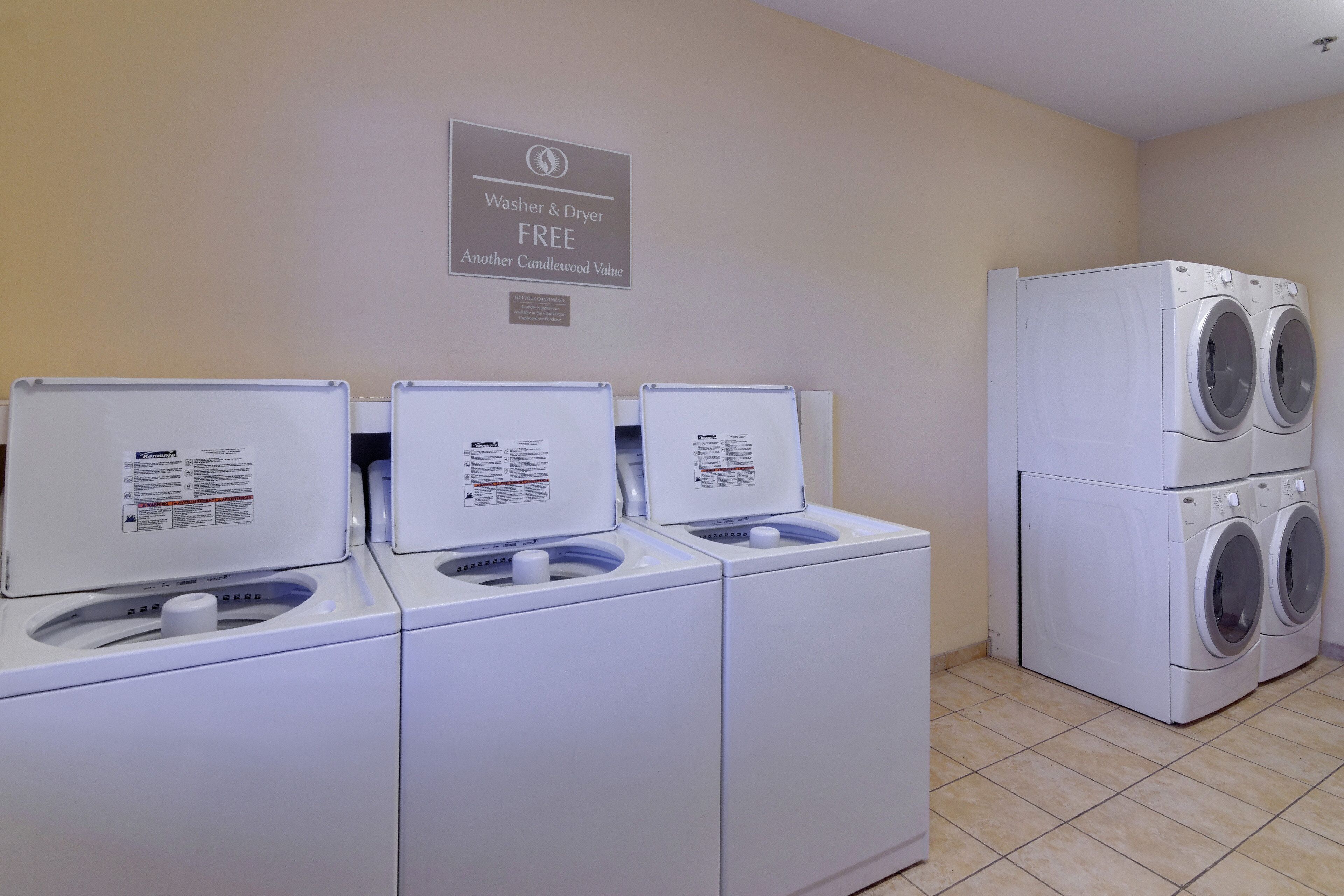 A laundry area with three Kenmore washers and dryers, a sign indicating free washer and dryer use, and a wall-mounted sign above.