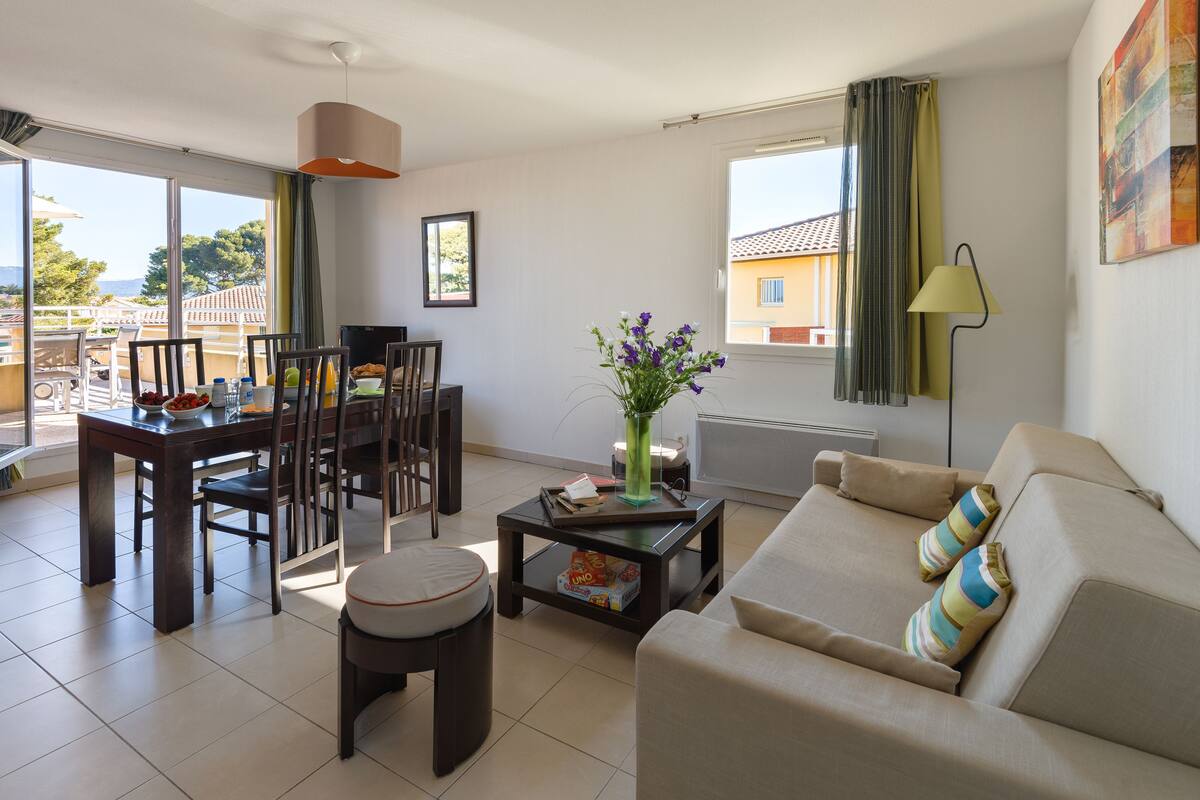 A modern living room with a dining area, large windows, and a view of the outside.