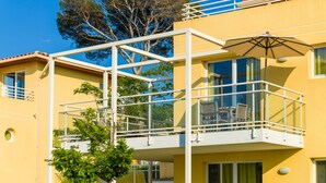 A yellow building with a balcony, a tree, and a clear blue sky.