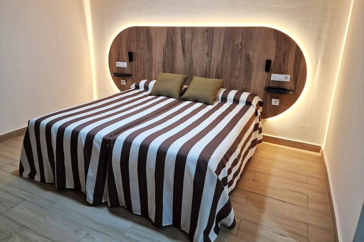 A neatly made bed with striped bedding, a wooden headboard, and bedside tables with wall-mounted lamps.
