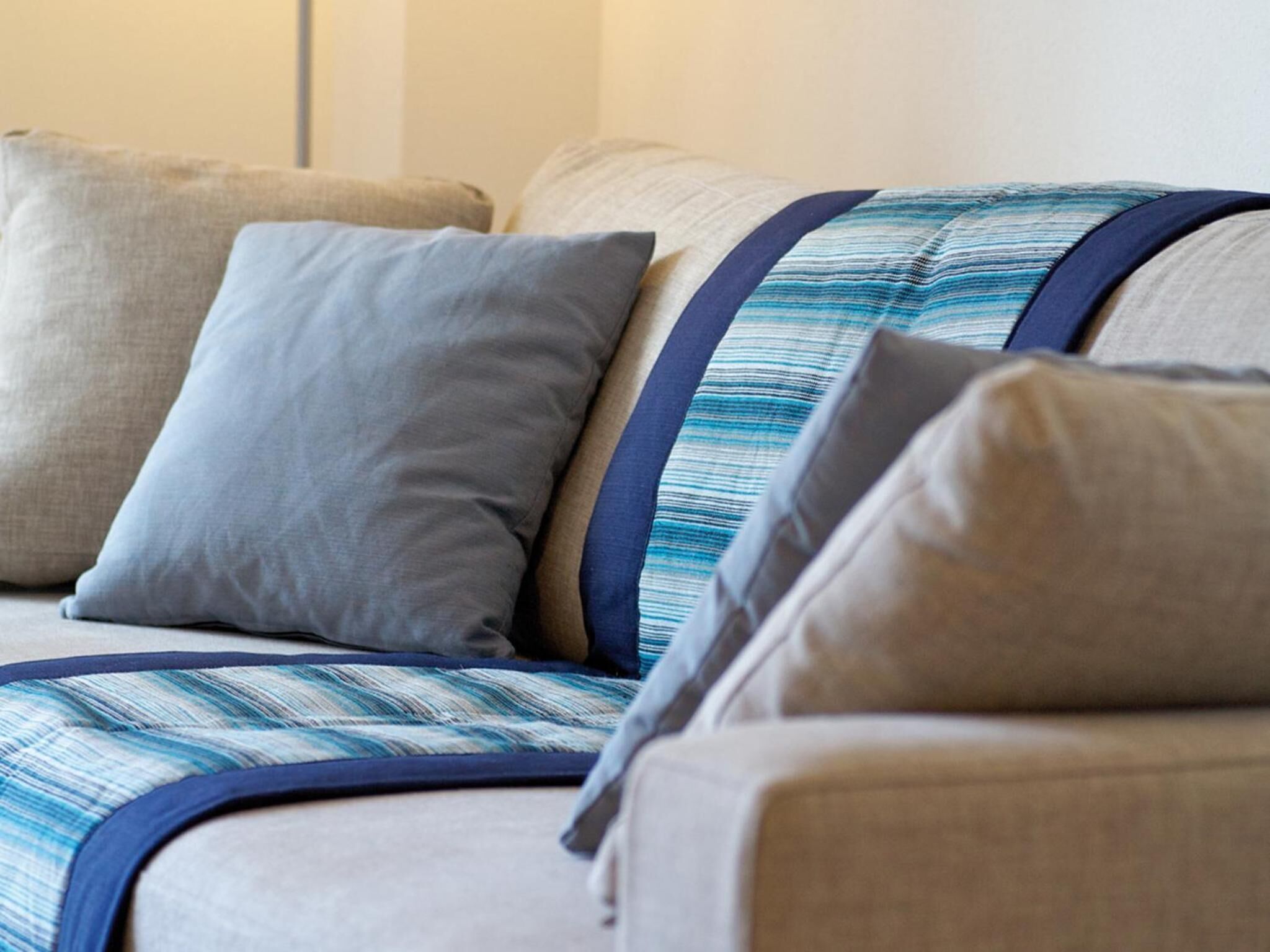 A sofa with a striped fabric and navy trim, accompanied by two pillows, one grey and one beige.