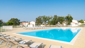 Una piscina con sillones de descanso, cielo despejado y edificios al fondo.