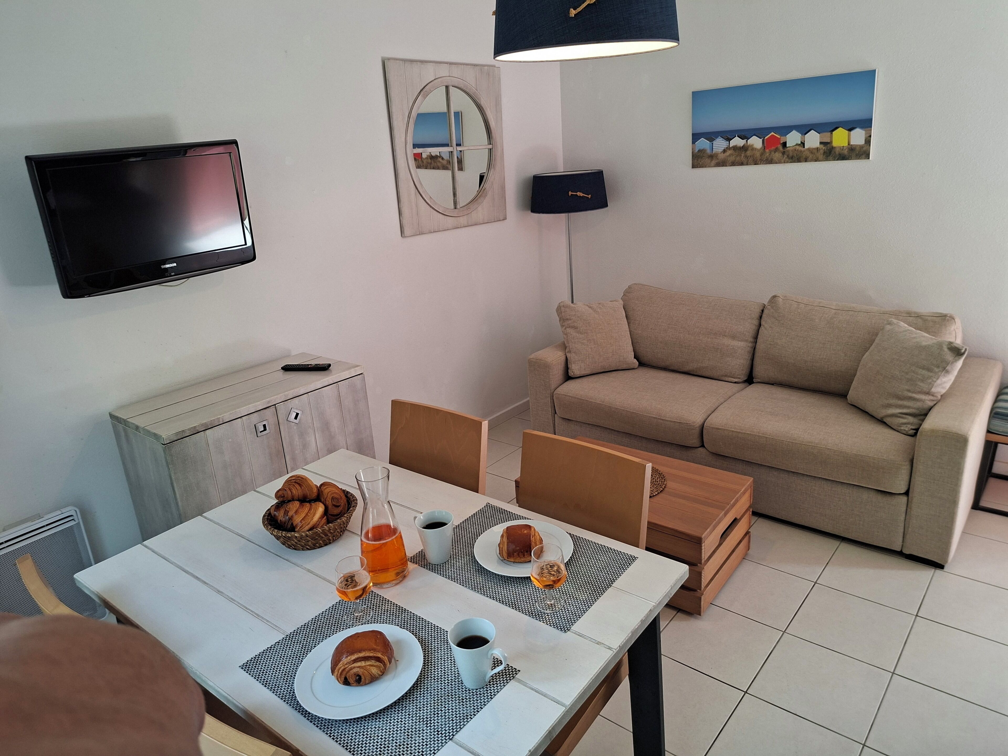 Una sala de estar con sofá, televisión, un cuadro y una mesa de comedor con comida y bebidas.