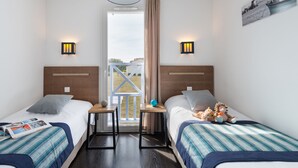 Habitación de hotel con dos camas, una ventana con vistas al exterior y una mesita entre ellas.
