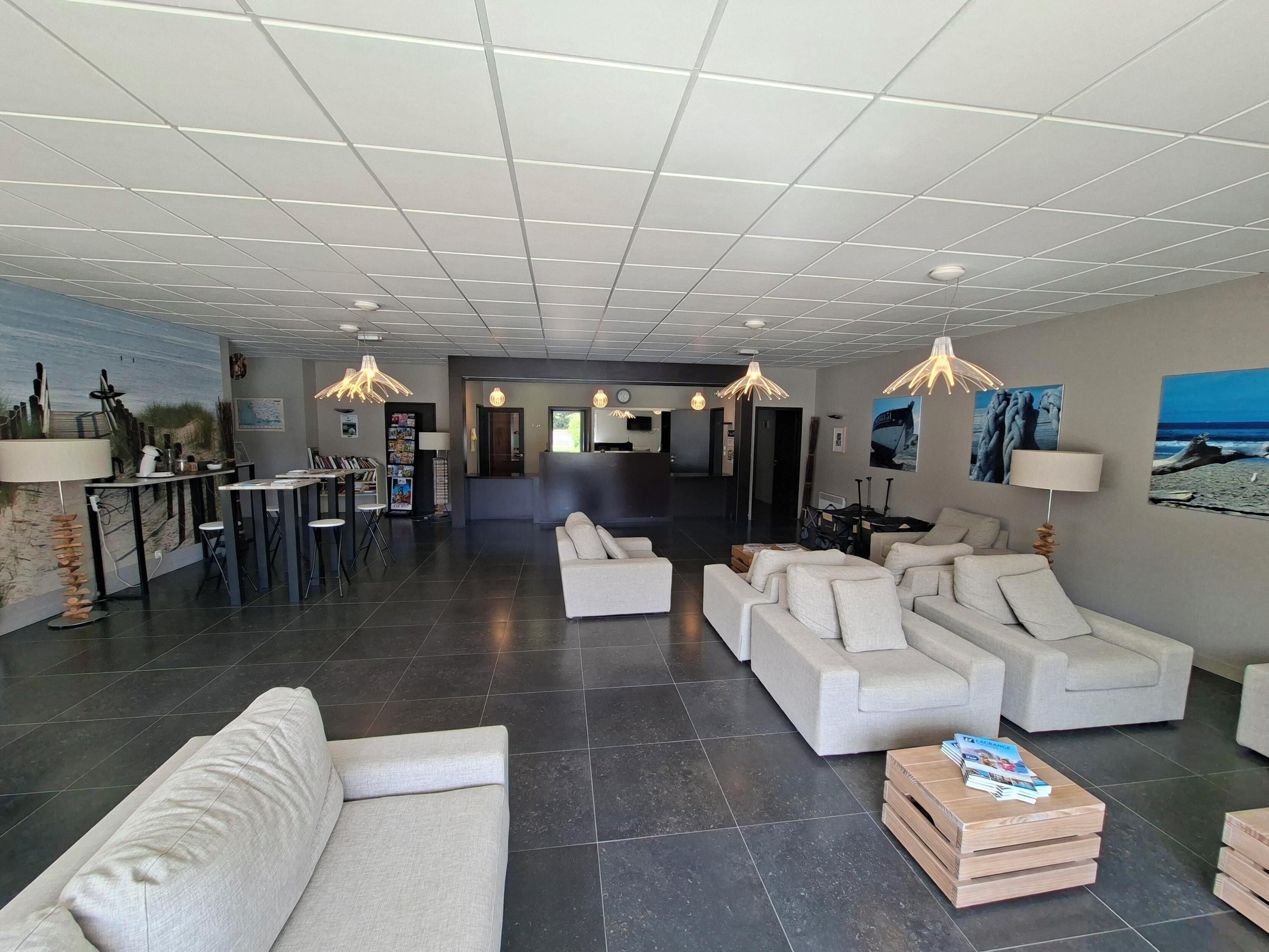 A modern hotel lobby with a reception desk, seating area with sofas, a coffee table, and artwork on the walls.