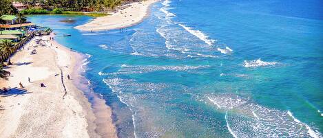 A beach with clear blue waters, a sandy shore, and a few people.