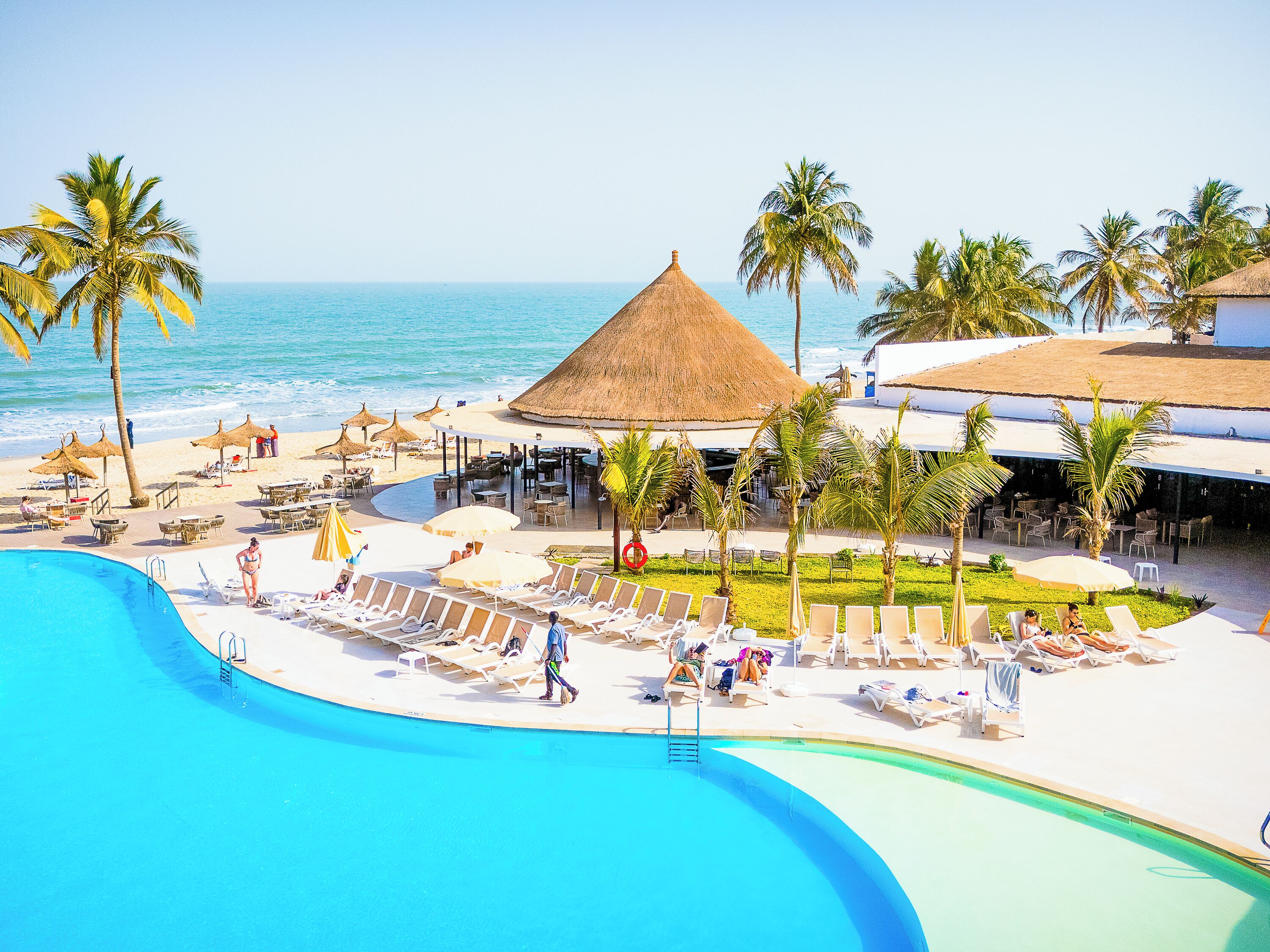 A resort with a swimming pool, beach area, and thatched-roof structures.