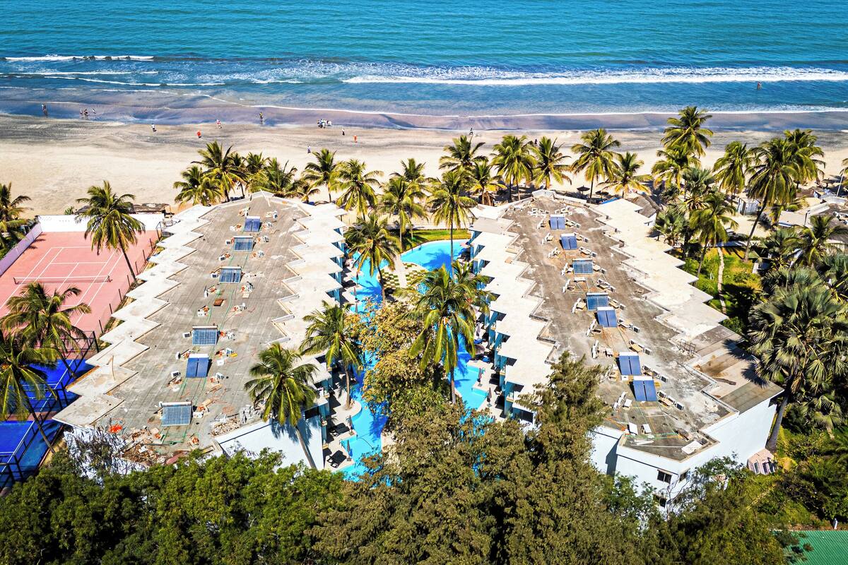 Vista aérea de un resort con piscina, playa y palmeras.