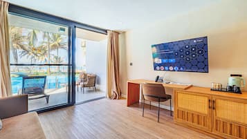 A hotel room with a large sliding glass door to a pool area, a TV on the wall, a wooden desk, and a comfortable seating area.