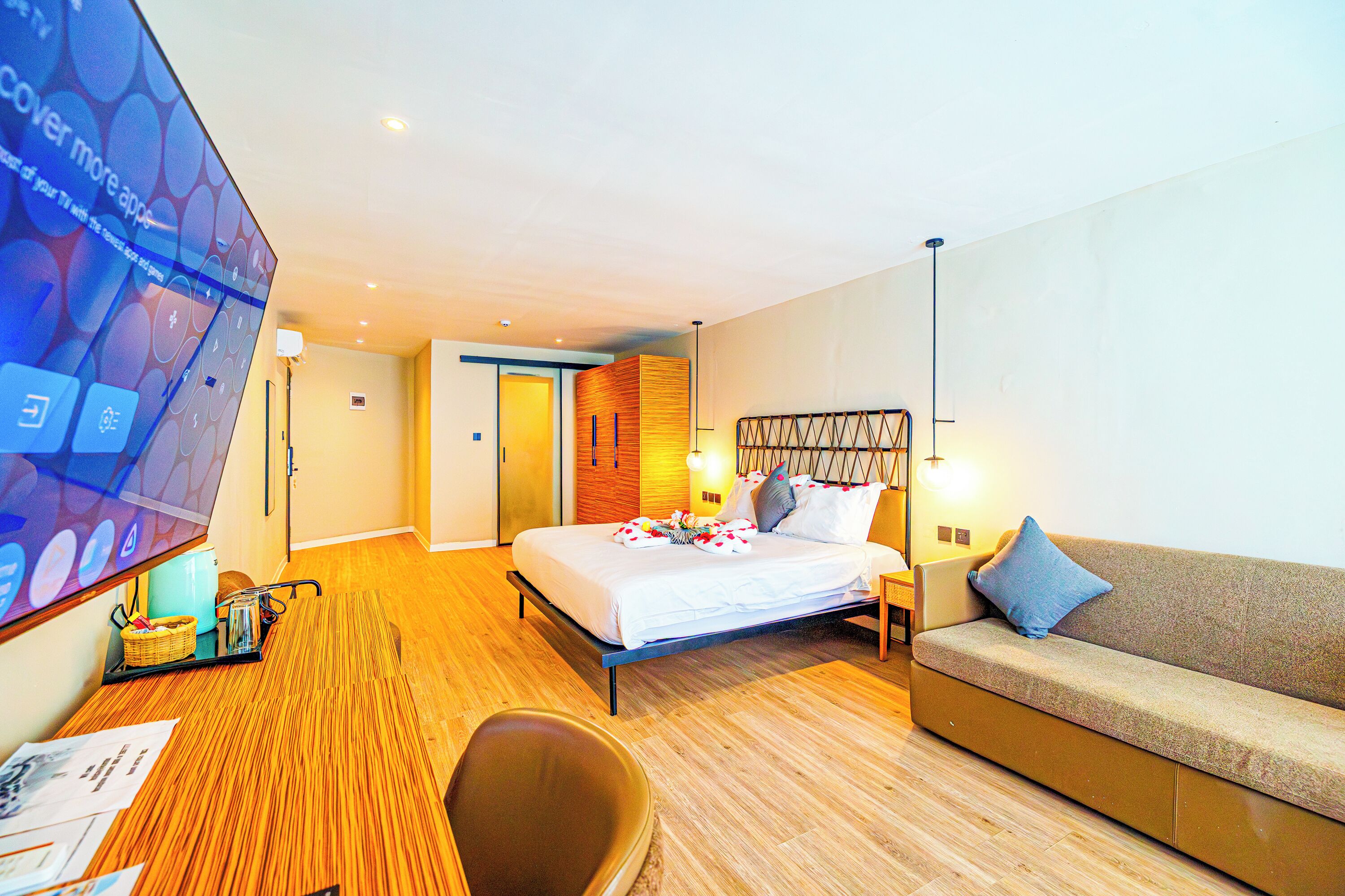 Una habitación de hotel moderna con una cama, un sofá, un escritorio con computadora y una pantalla de televisión.