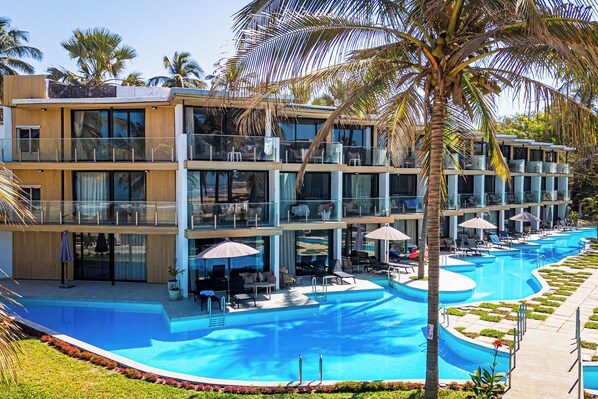 A modern hotel with a large pool, multiple balconies, and outdoor seating areas.